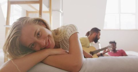 Relaxed Woman Smiling with Friends Playing Guitar in Background