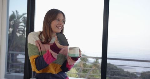 Woman in Colorful Sweater Talking on Smartphone and Holding Mug