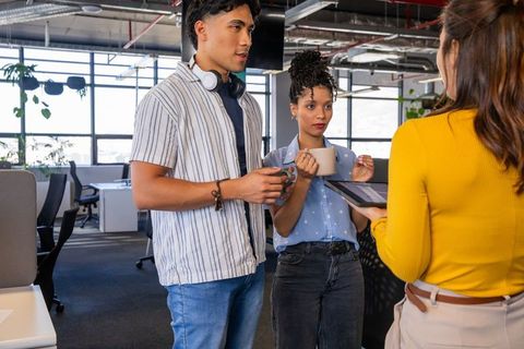 Diverse coworkers collaborating over tablet while holding coffee in bright modern office