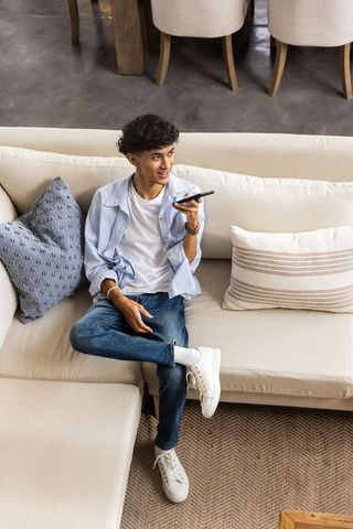 Man recording voice message on sofa in modern living room