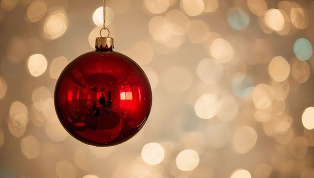 Hanging glossy red bauble reflecting warm bokeh lights and cozy holiday interior glow