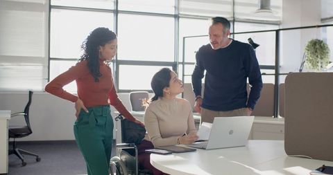 Multicultural team collaborating with employee in wheelchair at modern accessible office