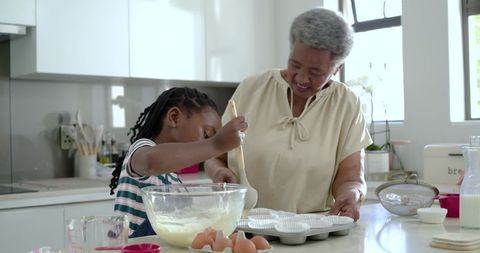 Grandparent and child baking together in sunlit kitchen, mixing batter for muffins