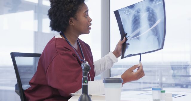 Female doctor in medical office examining X-ray film, pointing out areas of interest. Suitable for healthcare, radiology, medical diagnostics, and educational purposes related to medical training and professional healthcare settings.