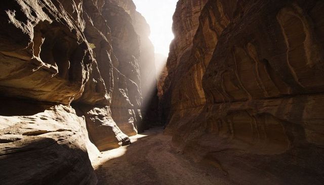 Sunbeam cutting through narrow sandstone slot canyon with layered striations and alcoves