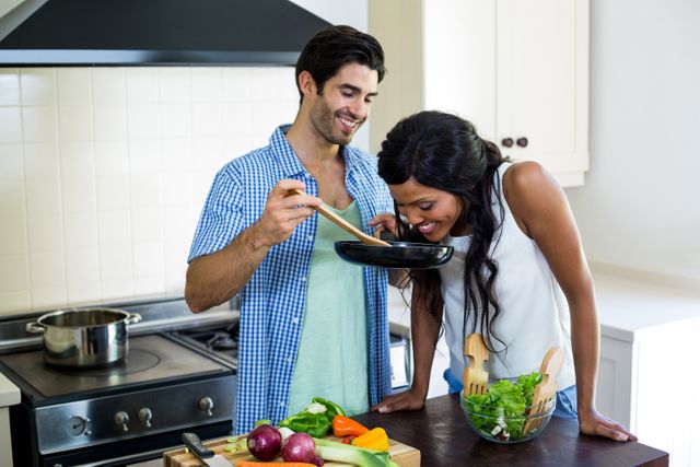 Young couple enjoying cooking together in a modern kitchen. They are preparing a meal with fresh vegetables and smiling, showcasing a moment of togetherness and bonding. Ideal for use in advertisements, blogs, or articles about healthy eating, relationships, home life, and culinary activities.