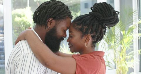 Couple embracing, touching foreheads in sunlit modern home sharing tender intimacy