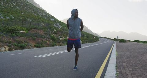 Athlete Stretching Pre-Run on Mountain Road in Hoodie