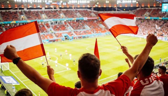 Passionate soccer fans raising arms and waving red white flags in stadium under floodlights
