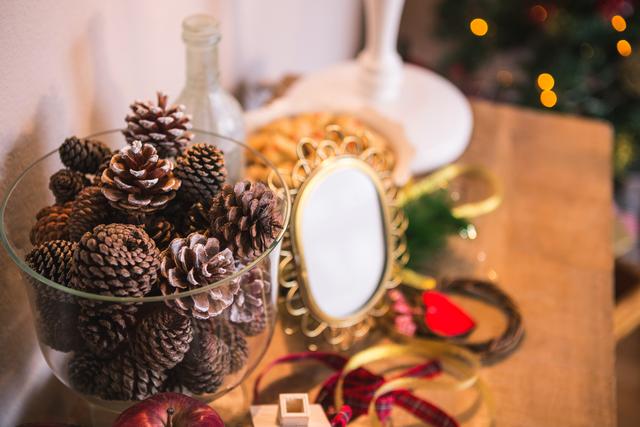 Pine cones in a glass bowl surrounded by Christmas decorations, including ribbons and ornaments. Ideal for holiday-themed content, festive home decor ideas, and seasonal greeting cards.