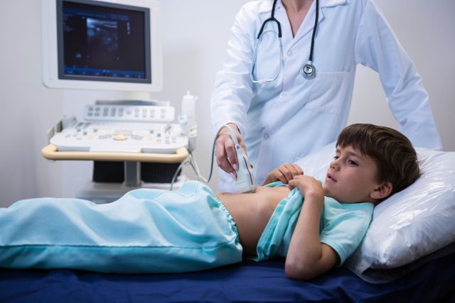 Female doctor performing ultrasound on young boy in hospital. Medical professional using sonography equipment to examine child's abdomen. Suitable for healthcare, pediatric care, medical diagnostics, and hospital-related content.