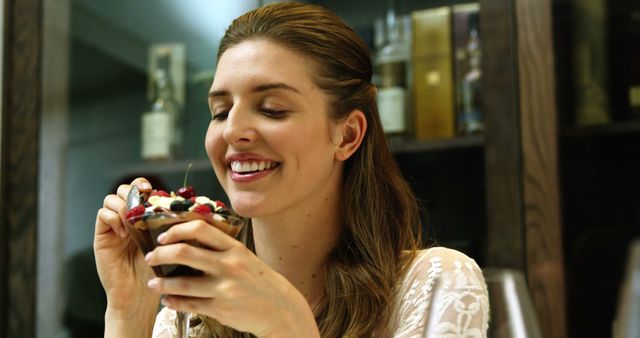 Woman smiling while enjoying a delicious dessert in a restaurant. Could be used for promoting desserts, restaurant menu items, happiness, indulgence, food blogs, culinary reviews, dining experiences, or lifestyle concepts celebrating special moments.
