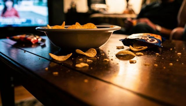 Cozy evening snacking with bowl of potato chips on wooden coffee table, open bag