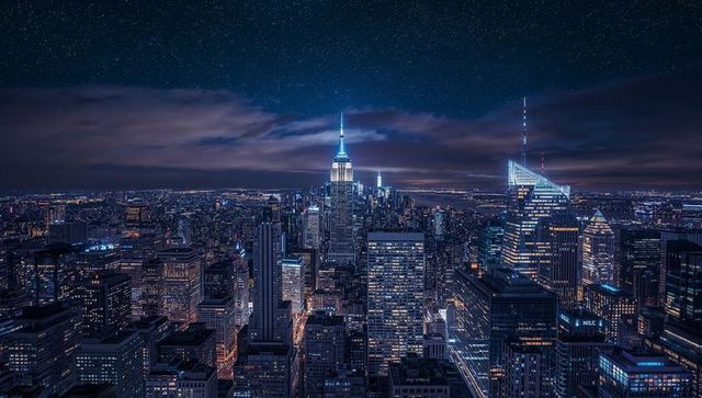 Empire State Building glowing spire anchoring neon-blue Manhattan skyline night rooftop aerial