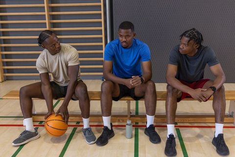 African american men sitting on gym bench holding basketball and resting during practice