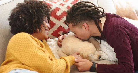 Couple cuddling golden retriever puppy on cozy sofa sharing tender kiss