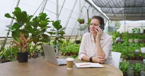 Woman Managing Greenhouse Business on Phone with Laptop