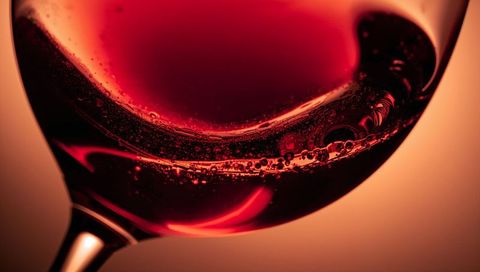 Macro closeup of red wine swirling in glass with bubbles and warm glowing backlight