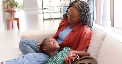 African mother cuddling smiling daughter on light sofa bonding at home lifestyle