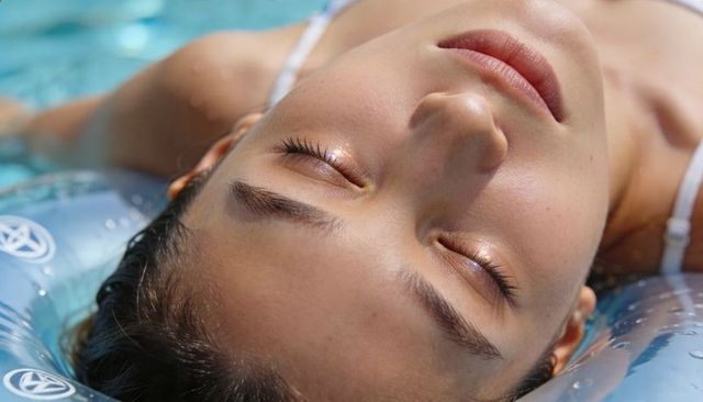 Asian woman floating on inflatable ring in sunlit pool closeup relaxing portrait