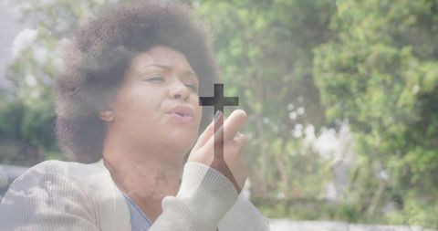 Contemplative woman holding cross in outdoor garden reflecting faith and inner peace