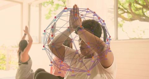 Practicing group yoga with focused woman pressing palms overhead in sunlit airy studio