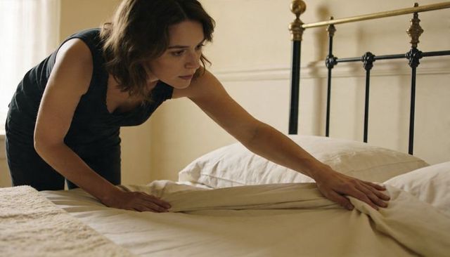 Woman smoothing bed sheets in minimal beige bedroom, making bed, calm morning routine