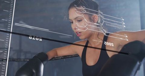 Young female boxer leaning on ring rope training with wearable analytics data hud overlay