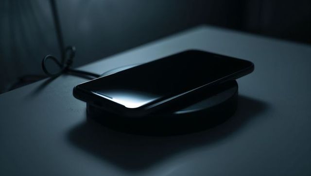 Sleek smartphone charging on wireless pad at night with reflective screen and coiled cable