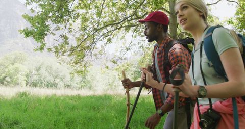 Diverse couple hiking through lush forest with backpacks