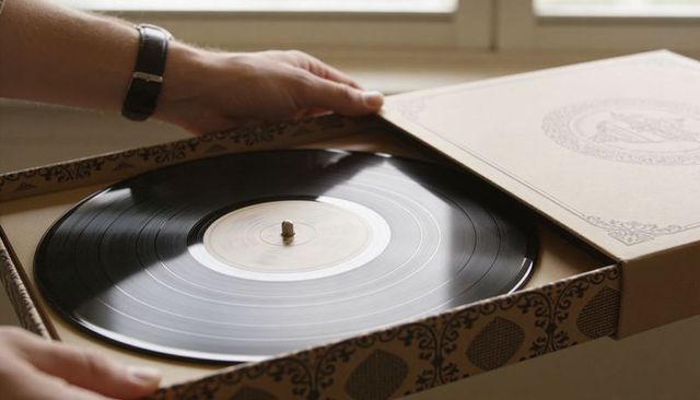 Hand removing vintage vinyl record from ornate cardboard case near window with wristwatch