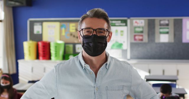 Portrait of caucasian male teacher wearing face mask in the class at school. hygiene and social distancing at school during covid 19 pandemic.