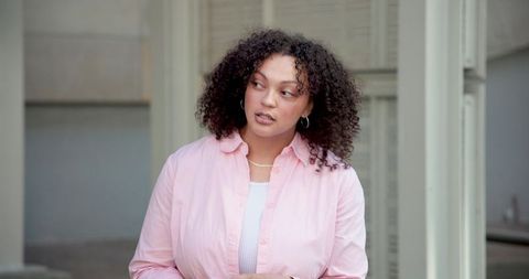 Thoughtful african american woman standing at doorway wearing pink shirt and hoop earrings