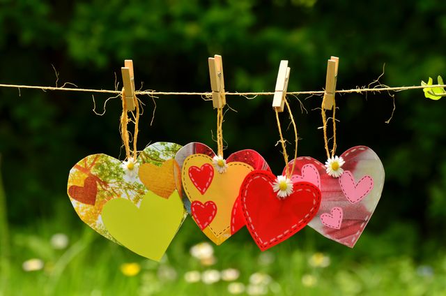 Close up view of colorful heart shaped decorations hanging on a clothesline with a blurred natural background. Each heart is designed with different patterns and colors. Ideal for illustrating concepts of love, holiday celebrations, romance, crafts, and decorations. Useful for Valentine's Day, wedding invitations, romantic social media posts, and festive event promotions.