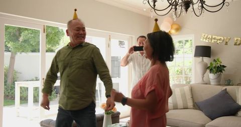 Chinese multigenerational family celebrating senior birthday in living room with party hats