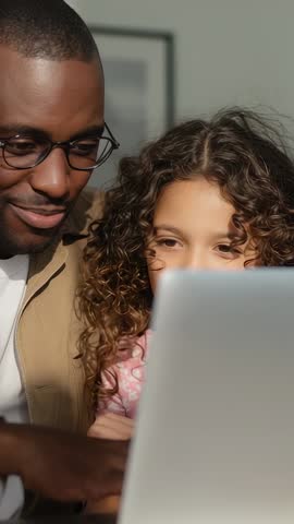 Vertical video smiling father guiding daughter on laptop, creating warm learning bond