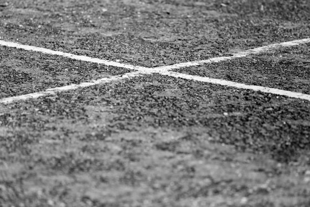 Engaging photograph of an urban pavement with a distinct cross mark on a rough asphalt surface. Perfect for use in design projects related to street photography, urban environments, road safety messaging, or background textures for graphics. Ideal for websites, brochures, or artistic illustrations needing a gritty and realistic urban texture.