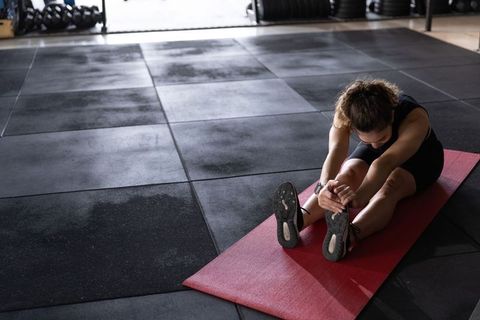 Female athlete stretching on red mat in gym for flexibility and recovery
