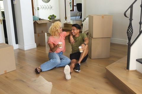 Interracial couple taking coffee break while unpacking in bright modern new home entryway