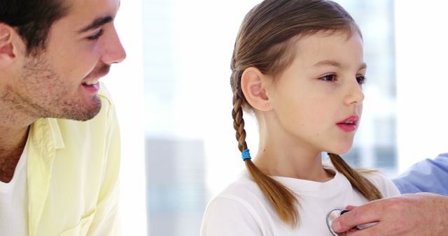 Father watching as doctor examines girl's heartbeat with stethoscope, highlighting trust and care in medical setting. Use for topics related to family health, medical check-ups, pediatric care, healthcare services, parental involvement in health.