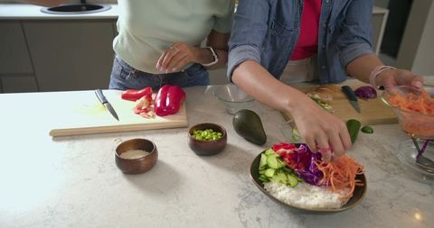 Diverse friends preparing colorful rice and vegetable bowls on marble island with avocado