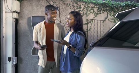 African American Couple Engaging with Technology Next to Electric Vehicle