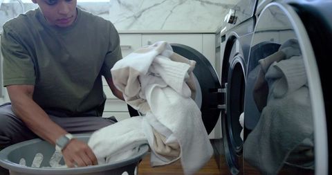 African american man sorting towels from front-load washer in modern laundry room