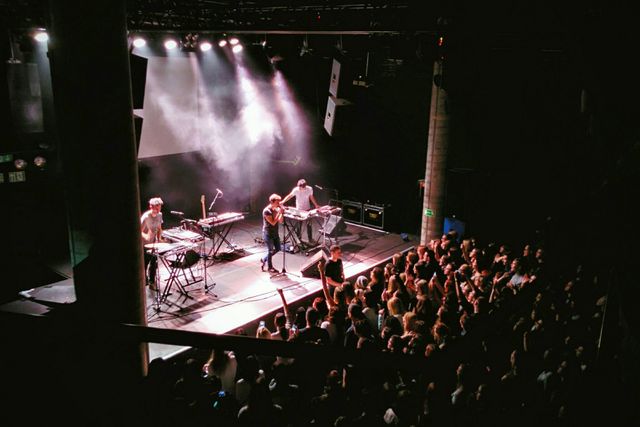 A dynamic scene depicting an indie band performing on stage at a concert venue, with a captivated audience watching. The performers are surrounded by musical equipment under various stage lights, creating an energetic atmosphere. This image can be used for promoting live music events, concert venues, band tours, music festivals, or any event related to music and entertainment. It highlights the excitement and energy of live performances.