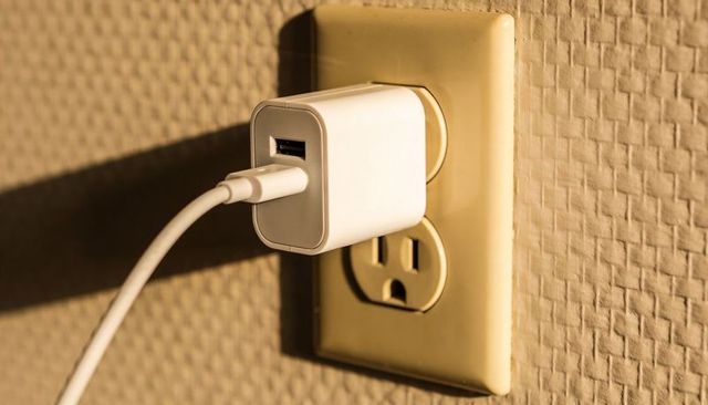 White USB Charger Plugging into Beige Wall Outlet Casting Diagonal Shadow