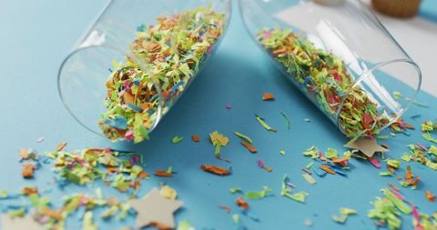 Champagne glasses spilling colorful confetti on blue background