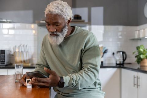Senior african american man checking health device and smartphone at kitchen counter