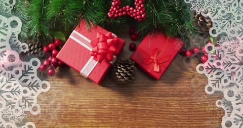 Red gift boxes under evergreen branches on wooden table with snowflake border, pine cones and berrie