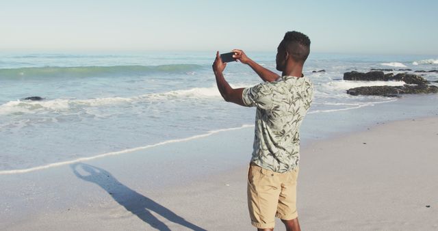 African american man with smartphone on sunny beach taking photos of the sea - Download Free Stock Photos Pikwizard.com