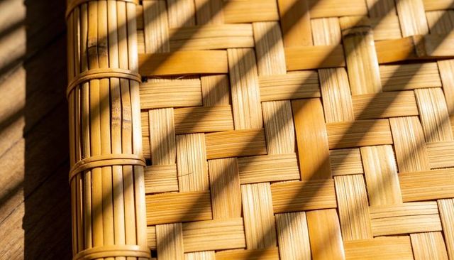 Woven bamboo mat casting diagonal sunlight shadows on warm wood surface